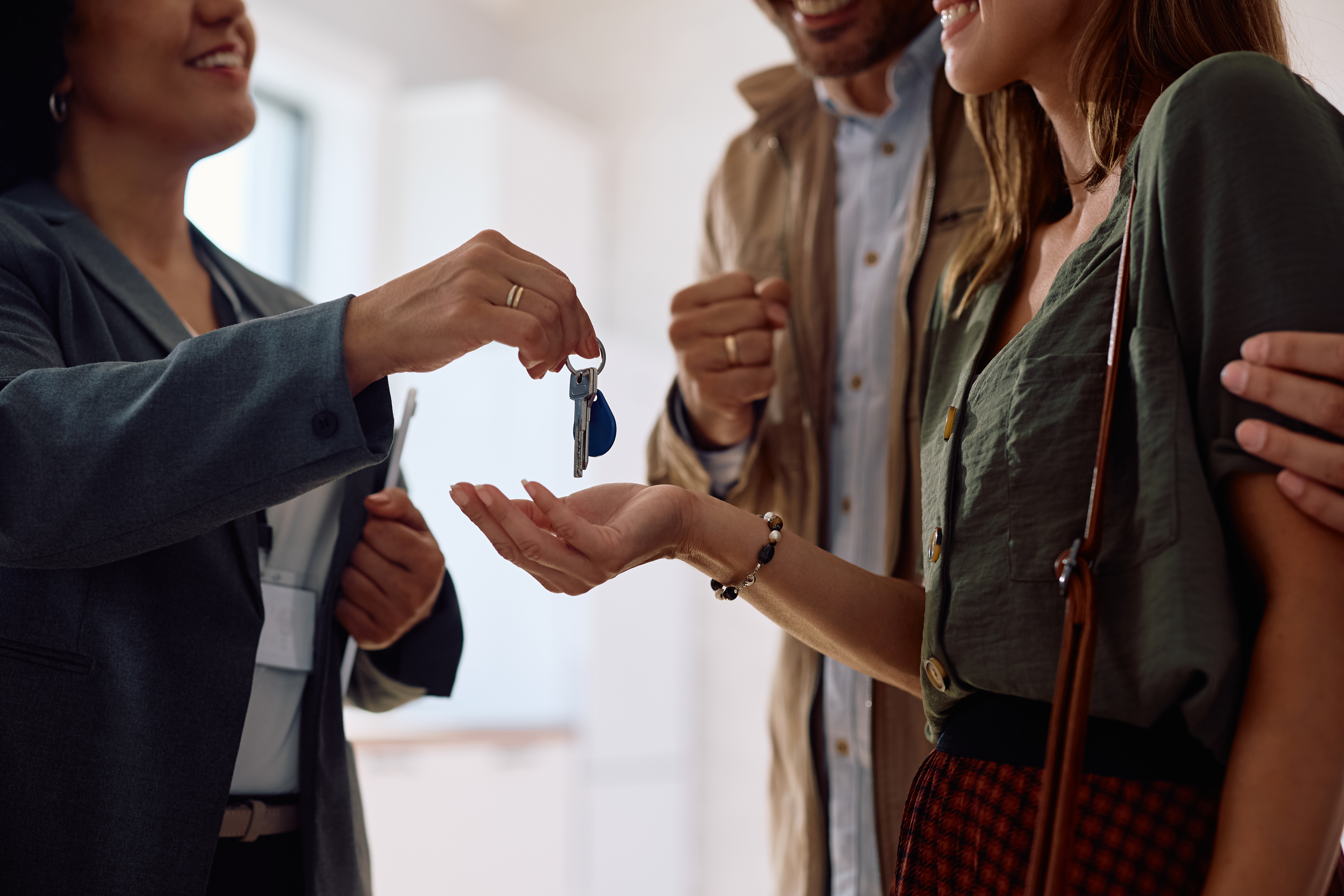 Close up of three people smiling while one person hands a set of key to another